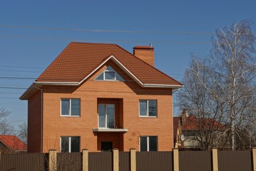 brick private brown house behind a fence on a sky background