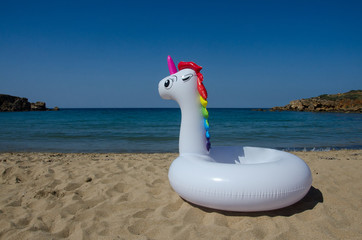 Inflatable unicorn float on sand near sea.  Summer holidays, beach vacation. Fantasy swim ring. Copyplace, place for text