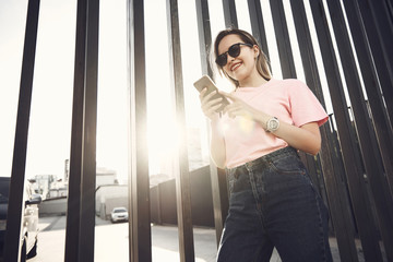Low angle portrait of beaming girl typing in contemporary mobile while standing over iron fence...