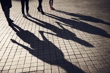 Close up females and men feet in modern shoes walking on sidewalk. Shadows locating opposite them