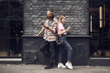 Full length outgoing male and smiling girl typing in modern mobiles while turning back to each other