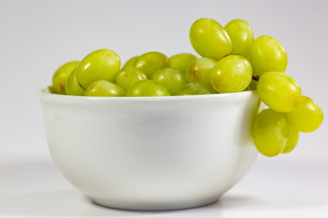 Green seedless grapes in a deep white bowl on a white tale waiting to be eaten