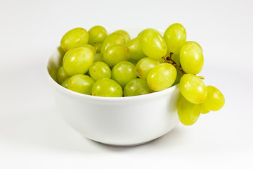 Green seedless grapes in a deep white bowl on a white tale waiting to be eaten