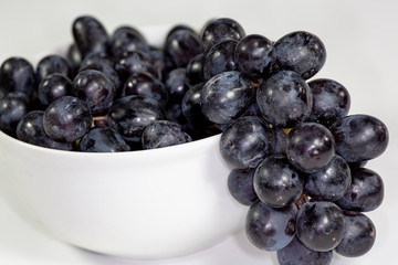 Black grapes in a deep white bowl on a white tale waiting to be eaten