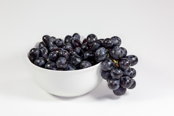 Black grapes in a deep white bowl on a white tale waiting to be eaten