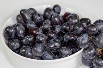 Black grapes in a deep white bowl on a white tale waiting to be eaten