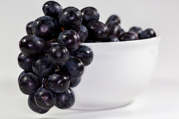 Black grapes in a deep white bowl on a white tale waiting to be eaten