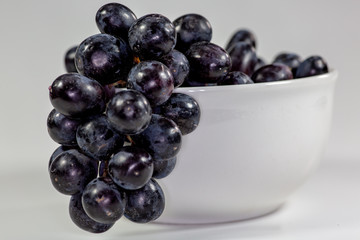 Black grapes in a deep white bowl on a white tale waiting to be eaten