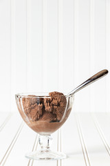 Fototapeta premium Vertical portrait of Chocolate Ice Cream in a glass dessert dish, with a metal spoon, on a white tabletop with a white background 