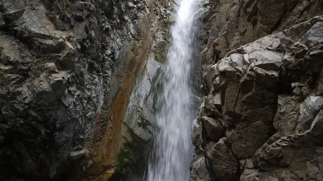 Pan down a cavernous waterfall as water falls down a narrow crevice to the bottom
