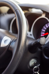 Close up modern black steering wheel, blurred dashboard, key and speedometer. Selective focus. Shallow depth of field.