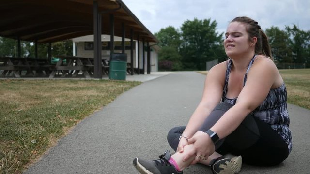 A jogging woman experiences ankle pain during a run in a park