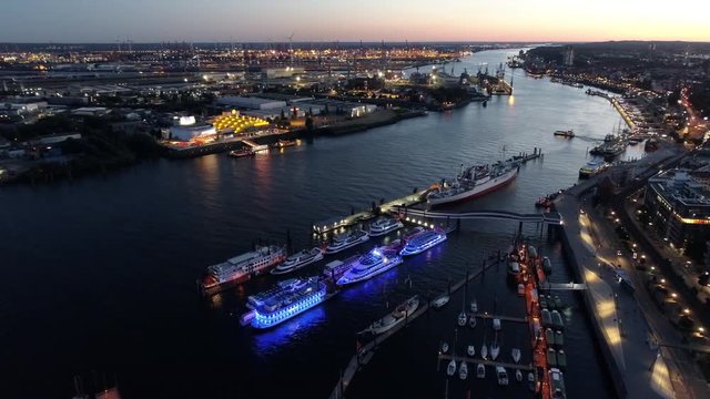 Aerial view of waterfront night illuminated view of Port of Hamburg, Germany. Downtown district city roads buildings office skyscrapers ferry terminal. Iluminated ships with blue lights at Elbe river.