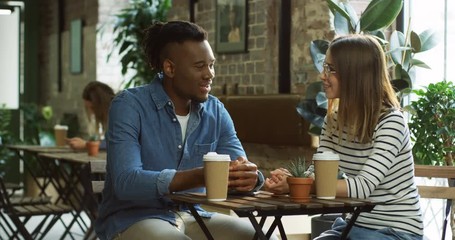 Portrait shot of the young multiethnical cheerful man and woman talking and drinking coffee in the loft cafe.
