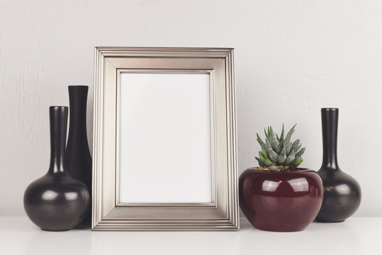 Blank silver frame, on a white table with aloe and vases. Mockup with copy space