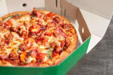 Delicious Italian pizza sliced with bacon, cheese, tomato, capsicum on wooden plate.