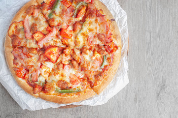 Delicious Italian pizza sliced with bacon, cheese, tomato, capsicum on wooden plate.