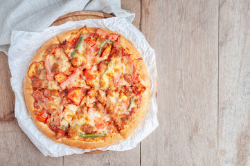 Delicious Italian pizza sliced with bacon, cheese, tomato, capsicum on wooden plate.
