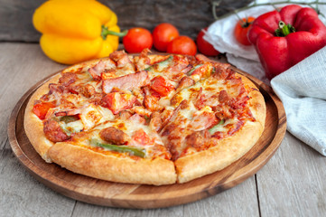 Delicious Italian pizza sliced with bacon, cheese, tomato, capsicum on wooden plate.