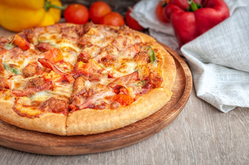 Delicious Italian pizza sliced with bacon, cheese, tomato, capsicum on wooden plate.