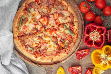 Delicious Italian pizza sliced with bacon, cheese, tomato, capsicum on wooden plate.
