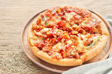 Delicious Italian pizza sliced with bacon, cheese, tomato, capsicum on wooden plate.