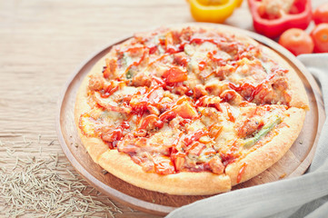 Delicious Italian pizza sliced with bacon, cheese, tomato, capsicum on wooden plate.