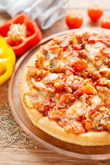 Delicious Italian pizza sliced with bacon, cheese, tomato, capsicum on wooden plate.
