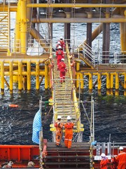 Construction crews are crossing gangway from accommodation vessel to wellhead platform.