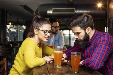 Young couple looking at mobile phone while sitting in local pub and drinking beer