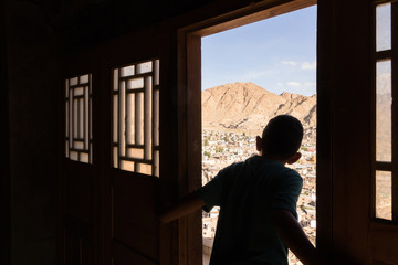 Naughty boy looking through the wooden ancient door to old town of Leh city from Leh palace in Leh Ladakh, Jammu and Kashmir, India