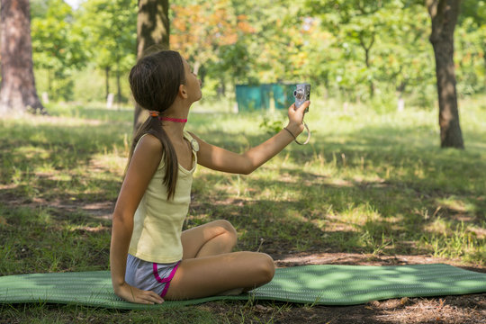 Little cute girl holding camera in hand and take a picture with selfie shot in park. beautiful eight-year-old girl in the park doing selfie