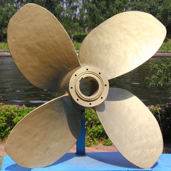 Large bronze ship propeller close-up on a pedestal in the summer against the water - sculpture in...