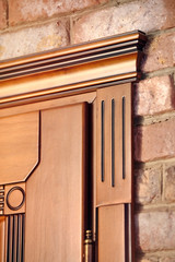 Element of a wooden door brown colored carved in classical style with golden hinges on brick wall...
