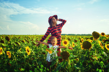 Happy loving family outdoors in summer. Young mother and daughter laughing and playing in the field with sunflowers