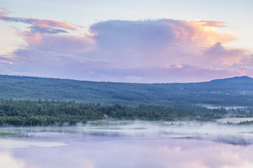 Nordic evening light over a lake with fog in a forest landscape
