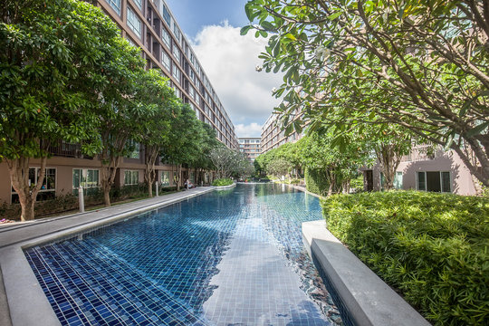 Swimming pool with green trees among high rise modern condominium building with pool on Phuket, Thailand