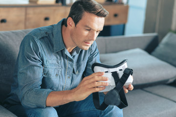 Virtual reality. Handsome nice pleasant man sitting on the sofa and holding 3d glasses while...