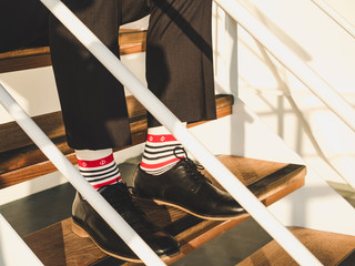 Men's legs in stylish, black shoes, dark pants and funny, bright, striped socks with a pattern on the deck of a cruise ship. Concept of lifestyle, fashion and fun