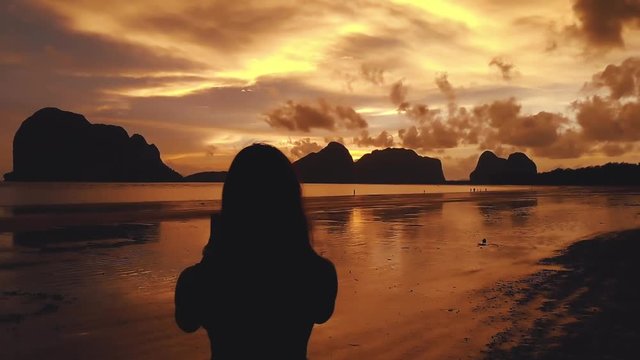 A young girl enjoys the view of the sea and the islands on the beach and takes pictures on the phone landscape. Silhouetted woman at sunset beach. Silhouettes at sunset. Thailand Asia Trang