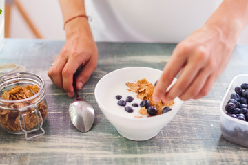 Obraz na płótnie Canvas A woman is eating yogurt with cereal and berries for breakfast, holding a spoon, close-up hands, a healthy diet and a diet concept, summer berries