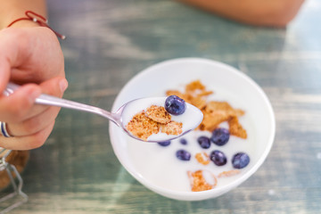 A woman is eating yogurt with cereal and berries for breakfast, holding a spoon, close-up hands, a healthy diet and a diet concept, summer berries