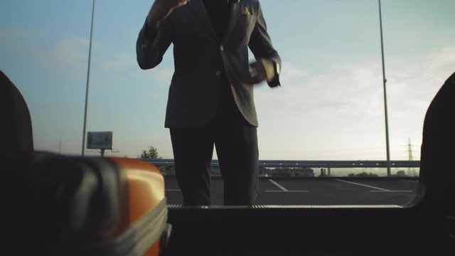 Man with blazer take out a case from car trunk.