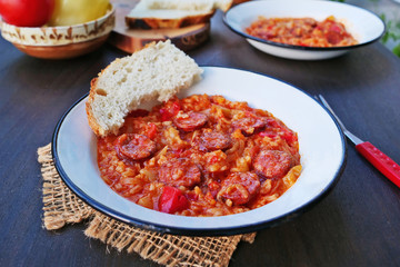 Vegetable stew, lecho with spicy sausage and rice in vintage enamel plates over dark wooden table
