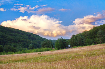 Fototapeta premium field against a background of mountain forests and beautiful clouds