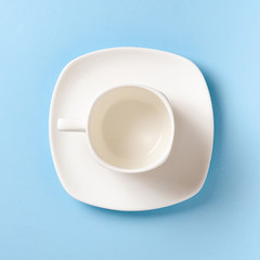 Empty white cup and saucer on a blue background. Flat lay concept