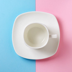 Empty white cup and saucer on a pink and blue background. Flat lay concept. Pastel shades