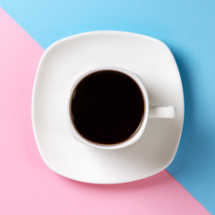 White cup with black coffee on a saucer. Pink and blue background. Flat lay concept. Pastel shades