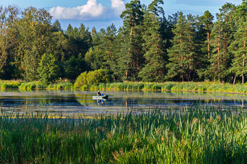 Fishermen in an inflatable boat in a large forest lake with a reed
