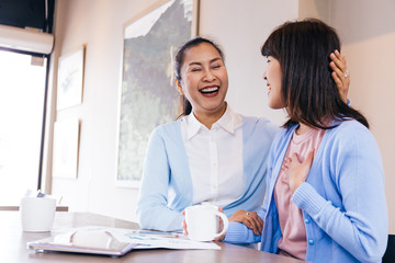 Asian family of middle aged woman and young teenage daughter talking and smiling at cafe restaurant